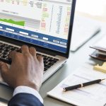 A person analyzes stock market data and financial charts on a laptop while working at a desk with an invoice and pen, reflecting the search for the best bank for investments to manage assets effectively.