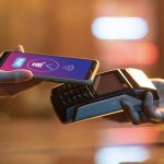 A person uses a smartphone to complete a contactless transaction on a card reader, illustrating the convenience and growing adoption of digital payments in modern retail environments.