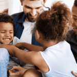 A happy family sitting together on a couch, with parents and children laughing and playing affectionately.