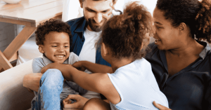 A happy family sitting together on a couch, with parents and children laughing and playing affectionately.