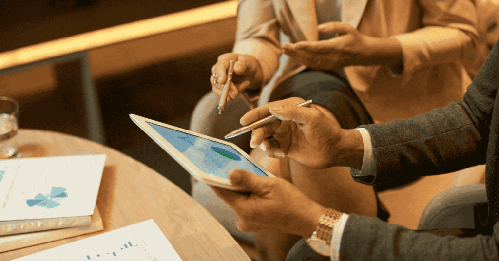 A businessman and businesswoman analyzing financial charts and graphs together at a glass desk in a modern office.