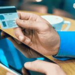 A person holding a credit card in front of a laptop while typing, representing online payment or e-commerce.